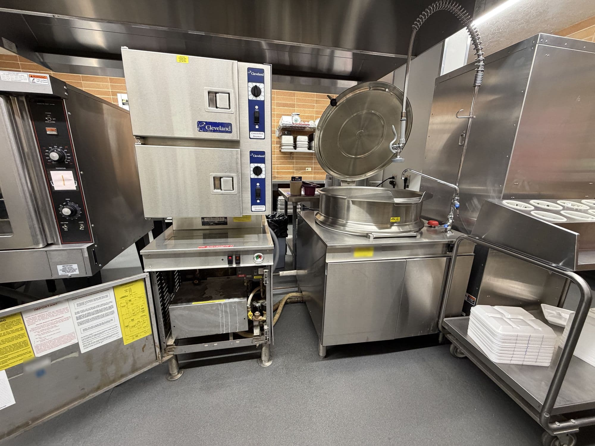 Stacked convection steamers beside a steam-jacketed kettle in an institutional kitchen